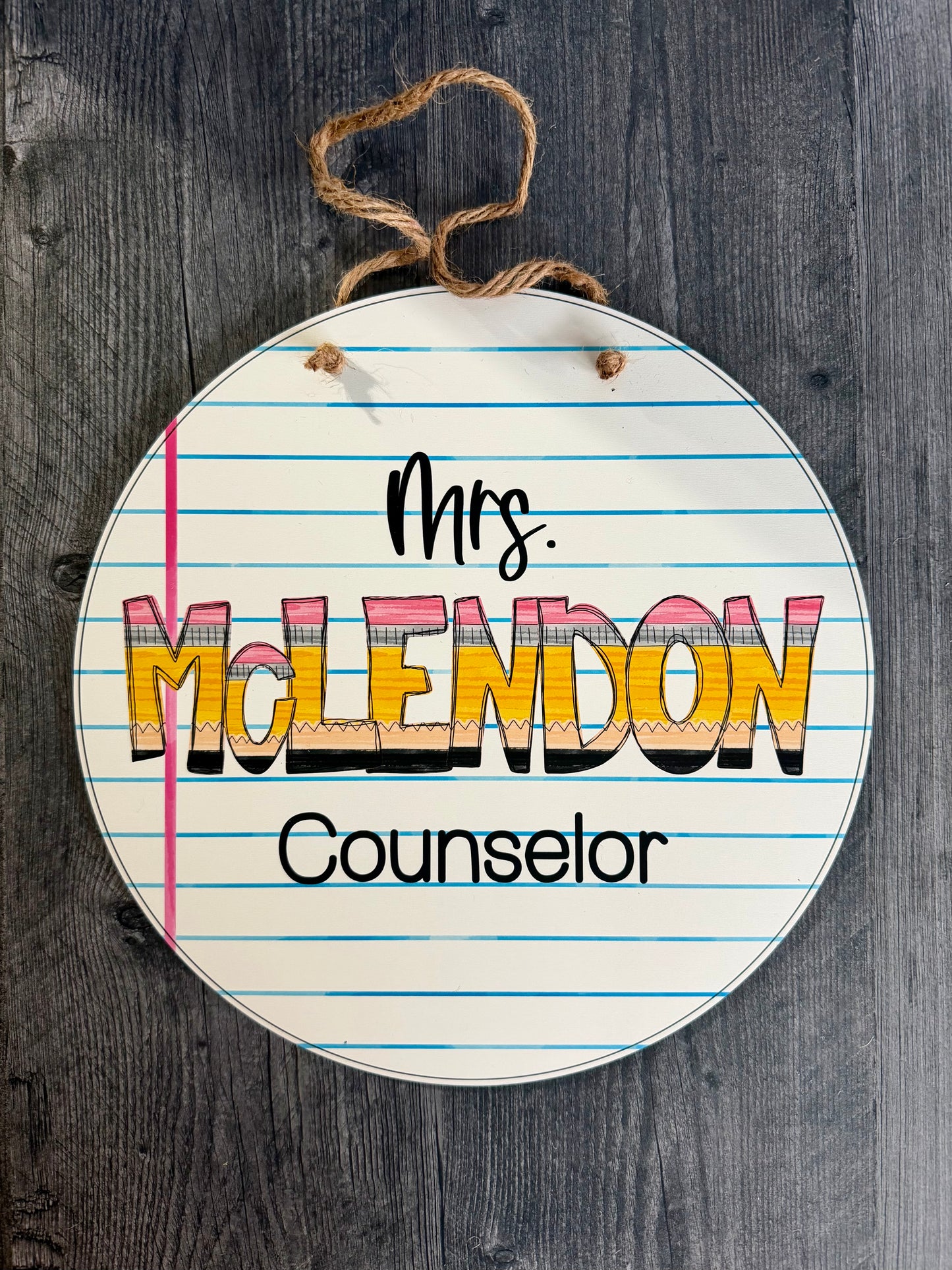 Round sign with lined paper design and 'Mrs. McLendon Counselor' text on a wooden background