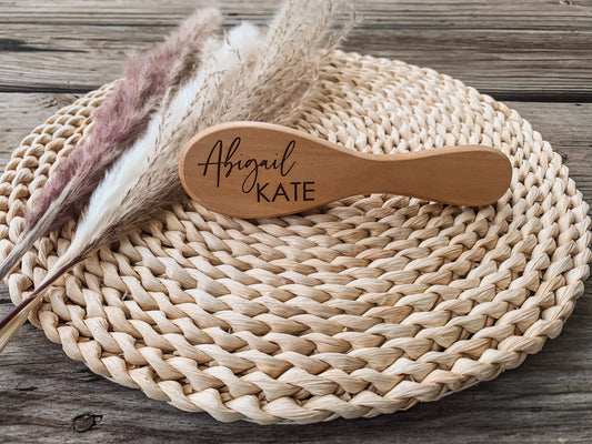 Wooden hairbrush with 'Abigail Kate' engraving on a woven mat with dried plants.