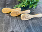 Three wooden hairbrushes with engraved names on a wooden surface with greenery.