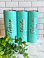 A set of three turquoise personalized engraved stainless steel tumblers with clear push-on lids, displayed on a countertop with a small green plant beside them.