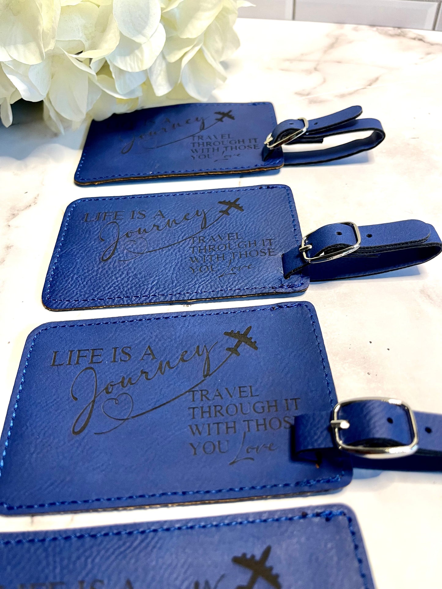 Several blue leatherette luggage tags. The tags have blue writing, and they say "Life is a journey. Travel through it with those you love."