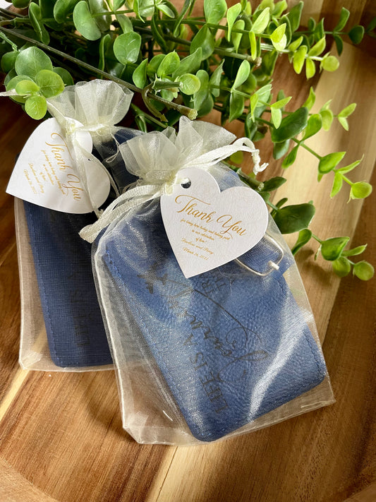 Two blue engraved leatherette luggage tags packaged in white organza bags. The bags have a Thank you tag attached.