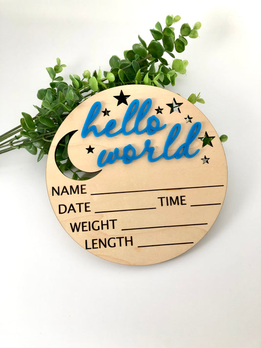 A wooden round sign with 'Hello World' text and a star pattern, alongside spaces for writing the name, date, time, and weight of the baby.
