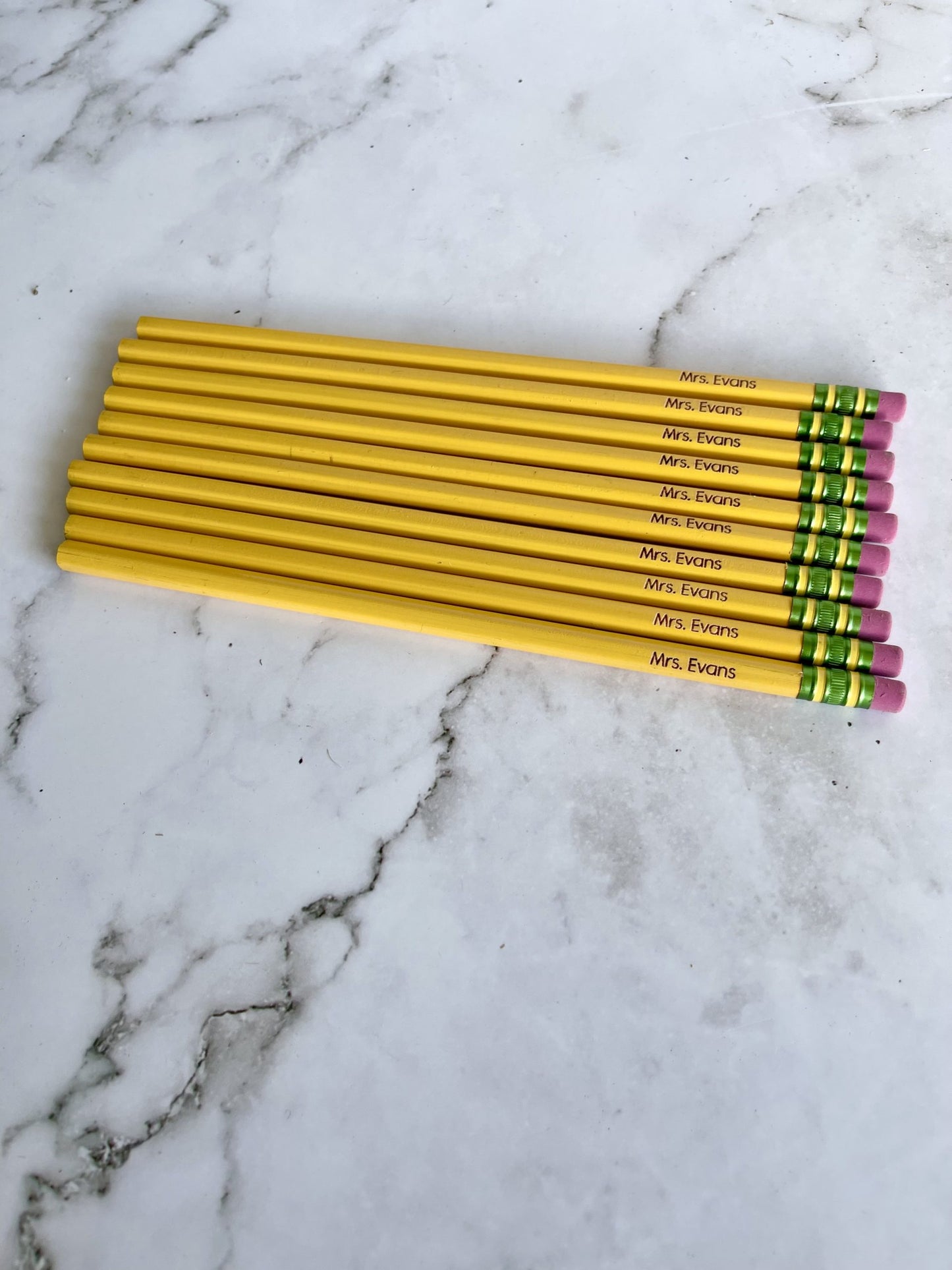 A set of yellow Ticonderoga pencils with orange erasers personalized with a name, placed on a marble surface.