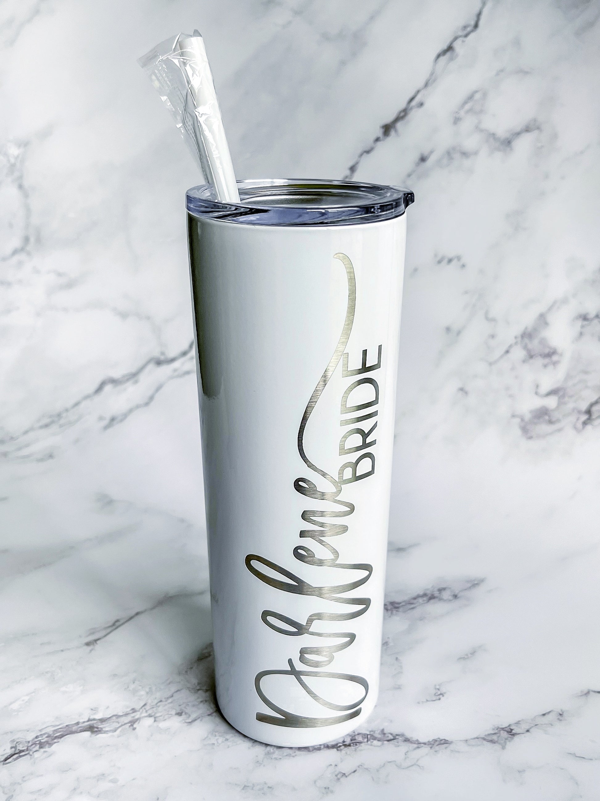 A white 20 oz. stainless steel tumbler with a clear push-on lid and a personalized engraved design that reads the bride's name and the bride label